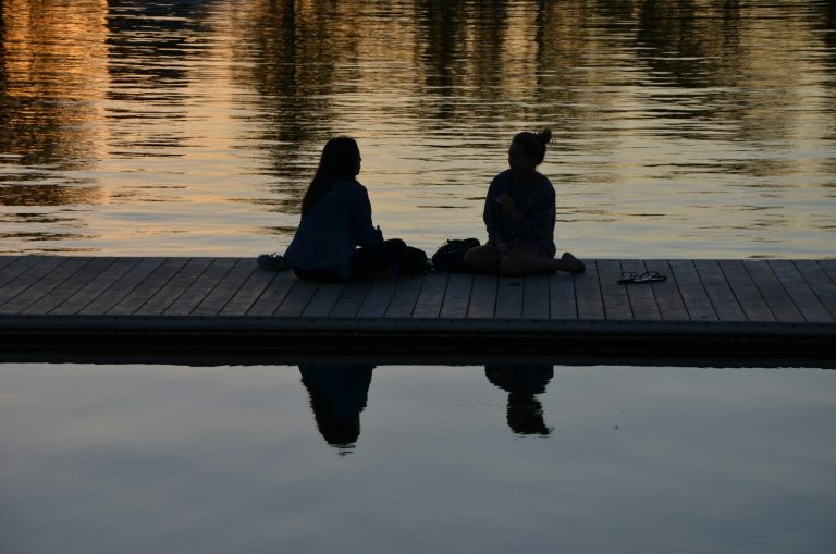 2 person sitting on dock during sunset